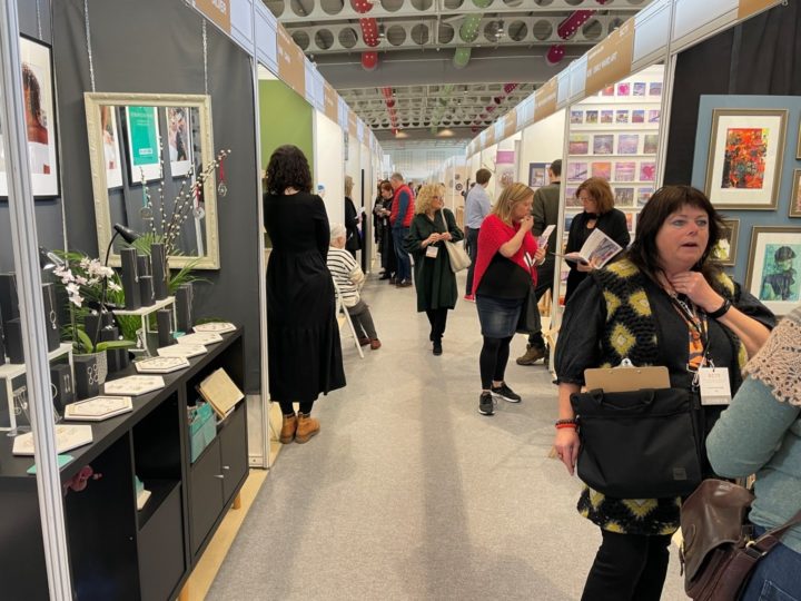 Visitors looking at exhibits and interacting between 2 rolls of stalls at the last British Craft Trade Fair